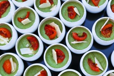 Petits contenants remplis de mousse verte garnie de morceaux de tomates confites et copeaux de fromage.