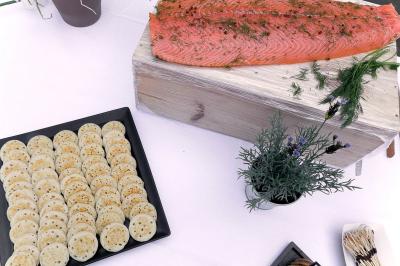 Saumon gravlax sur planche en bois avec un plateau de blinis et des herbes fraîches en décoration.