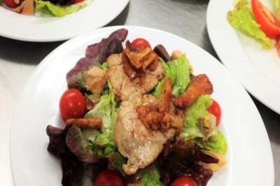 Assiette de salade garnie de feuilles vertes, tomates cerises, champignons et morceaux de viande grillée.