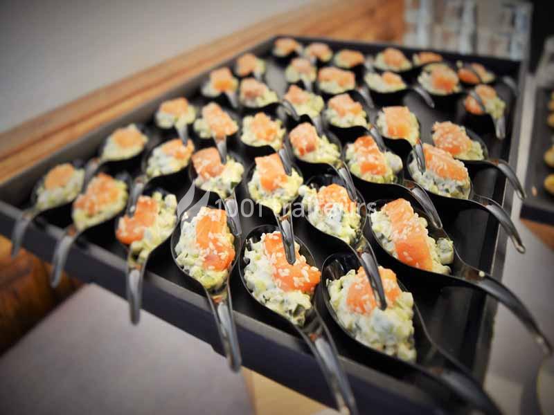 Cuillères apéritives garnies de tartare de saumon et d'une préparation crémeuse, disposées sur un plateau noir.