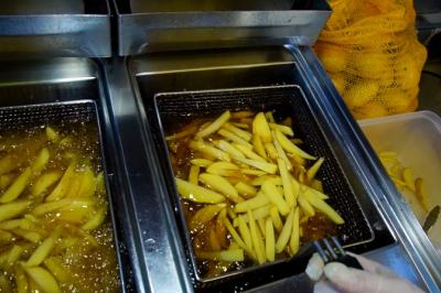 Frites en cours de cuisson dans une friteuse industrielle, avec des pommes de terre fraîches visibles à proximité.