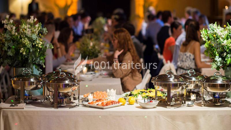 Buffet avec plats variés sur une table, entouré d'invités assis à des tables décorées de fleurs.