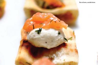 Canapé garni de fromage frais, saumon fumé et herbes, présenté sur une base de pain grillé.