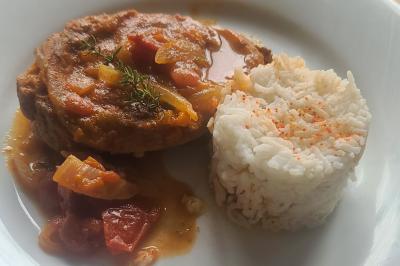 Assiette contenant une tranche de viande en sauce avec des légumes et un accompagnement de riz blanc saupoudré de paprika.