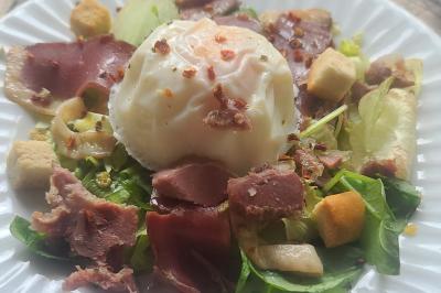 Salade composée avec œuf poché, magret de canard, croûtons, champignons et feuilles de salade verte.
