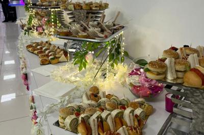 Buffet de mini-sandwichs variés et desserts disposés sur une table décorée de fleurs et de lumières.
