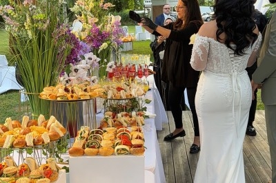 Buffet de réception en extérieur avec plats variés, fleurs décoratives et invités en tenue de cérémonie.