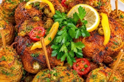Plat de poulet rôti avec rondelles de citron, pommes de terre croustillantes, tomates cerises et olives, garni de persil.