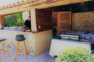 Homme préparant des plats dans une cuisine extérieure en bois et pierre, avec un comptoir et des tables aménagées.