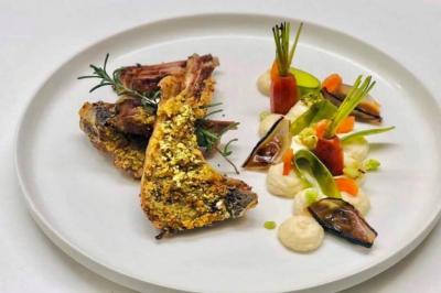 Carré d'agneau en croûte d'herbes accompagné de légumes finement dressés et purée sur une assiette blanche.