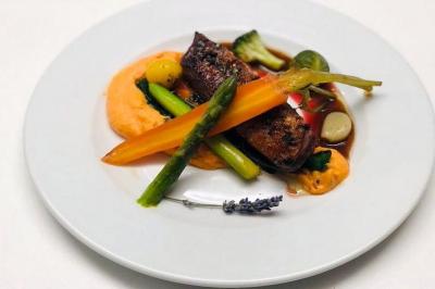 Assiette gastronomique avec viande, purée, légumes colorés et sauce, présentée sur une table blanche.