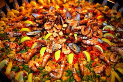 Plat de paella garnie de crevettes, moules, calamars, légumes colorés et quartiers de citron.