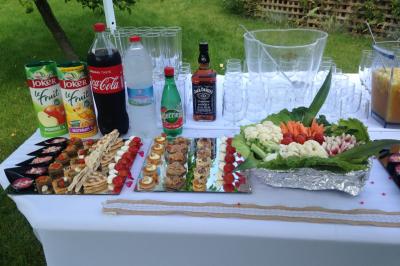 Buffet en extérieur avec boissons, verrines, toasts variés et plateau de crudités sur une table blanche.