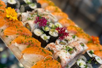 Plateau de sushis variés avec makis, nigiris au saumon et garnitures de fleurs comestibles et ciboulette.