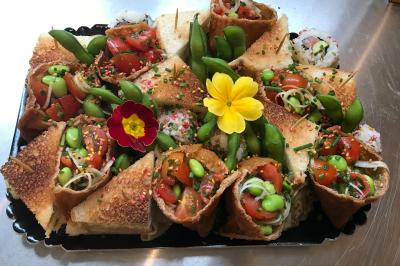 Plateau de bouchées variées comprenant des rouleaux garnis de légumes, des tranches de pain grillé et des fleurs comestibles.