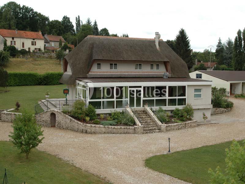 Maison traditionnelle avec toit de chaume, entourée d'un jardin, d'une terrasse et d'une allée gravillonnée.