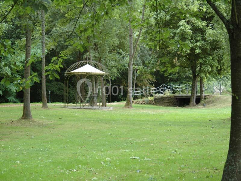Un kiosque en métal au centre d'une pelouse entourée d'arbres dans un parc verdoyant.
