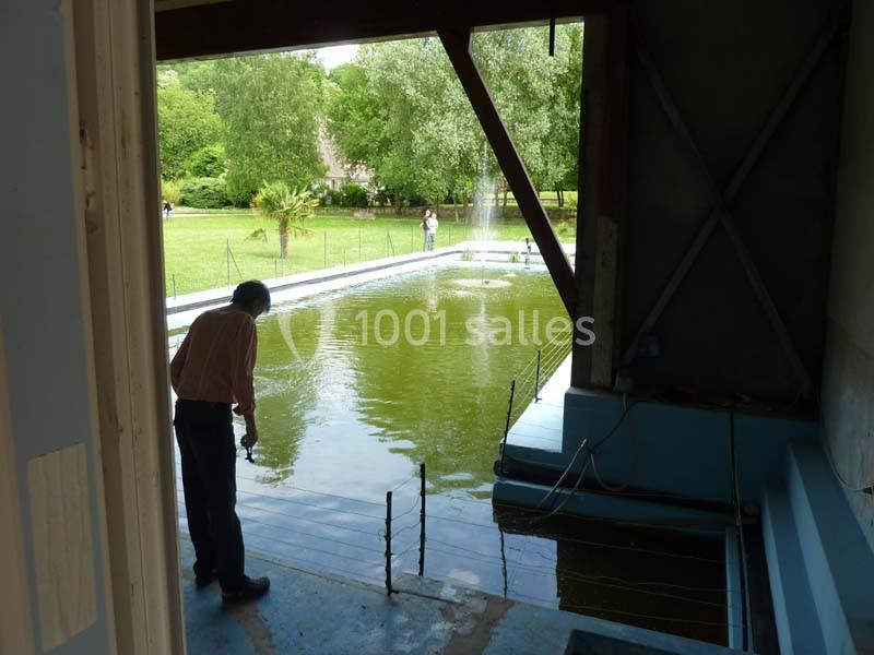 Un homme observe un bassin rectangulaire rempli d'eau, ouvert sur un jardin verdoyant en arrière-plan.