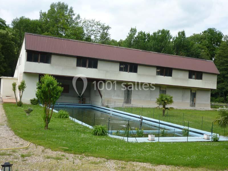 Bâtiment rectangulaire à toit rouge, entouré de verdure, avec un bassin rectangulaire au premier plan.