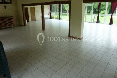 Salle décorée pour un événement avec tables dressées, chandeliers, nappes blanches et buffet garni en arrière-plan.