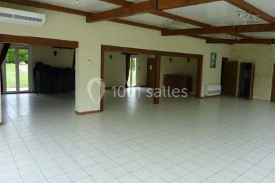 Salle décorée pour un événement avec tables dressées, chandeliers, nappes blanches et buffet garni en arrière-plan.