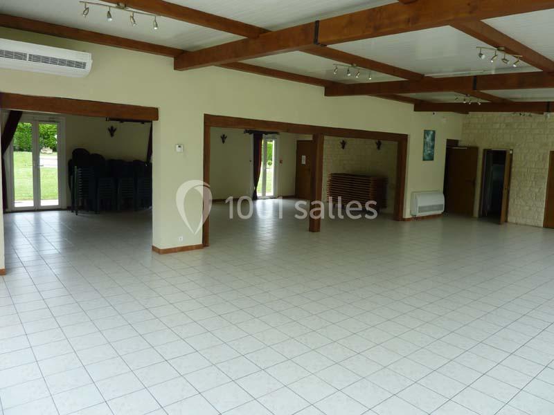 Salle spacieuse avec carrelage clair, poutres apparentes et grandes ouvertures donnant sur l'extérieur.