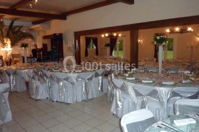 Salle décorée pour un événement avec tables dressées, chandeliers, nappes blanches et buffet garni en arrière-plan.