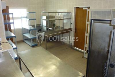 Salle décorée pour un événement avec tables dressées, chandeliers, nappes blanches et buffet garni en arrière-plan.