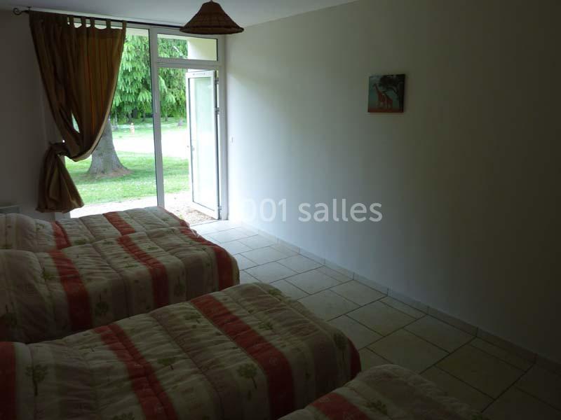 Chambre avec plusieurs lits simples, carrelage au sol, grande porte vitrée ouverte sur un jardin verdoyant.