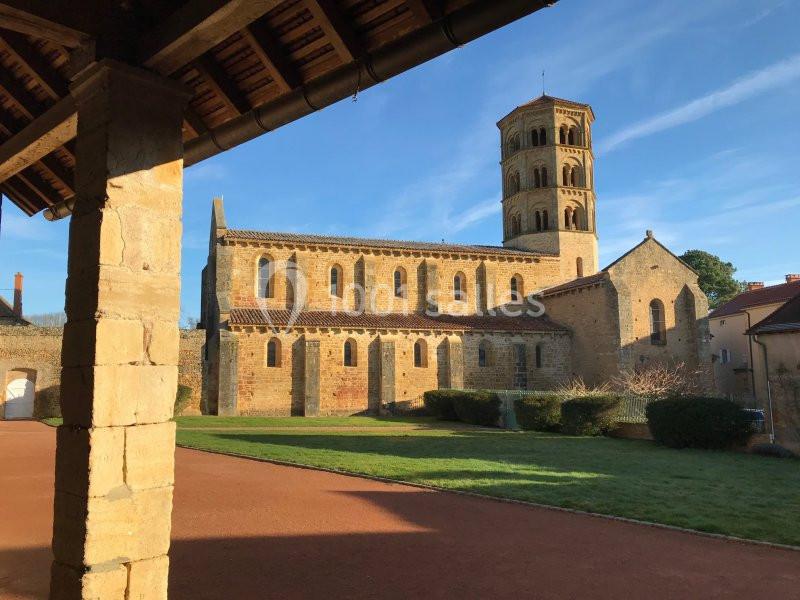 Église en pierre avec clocher à plusieurs niveaux, vue depuis une cour ensoleillée avec pelouse et allée.