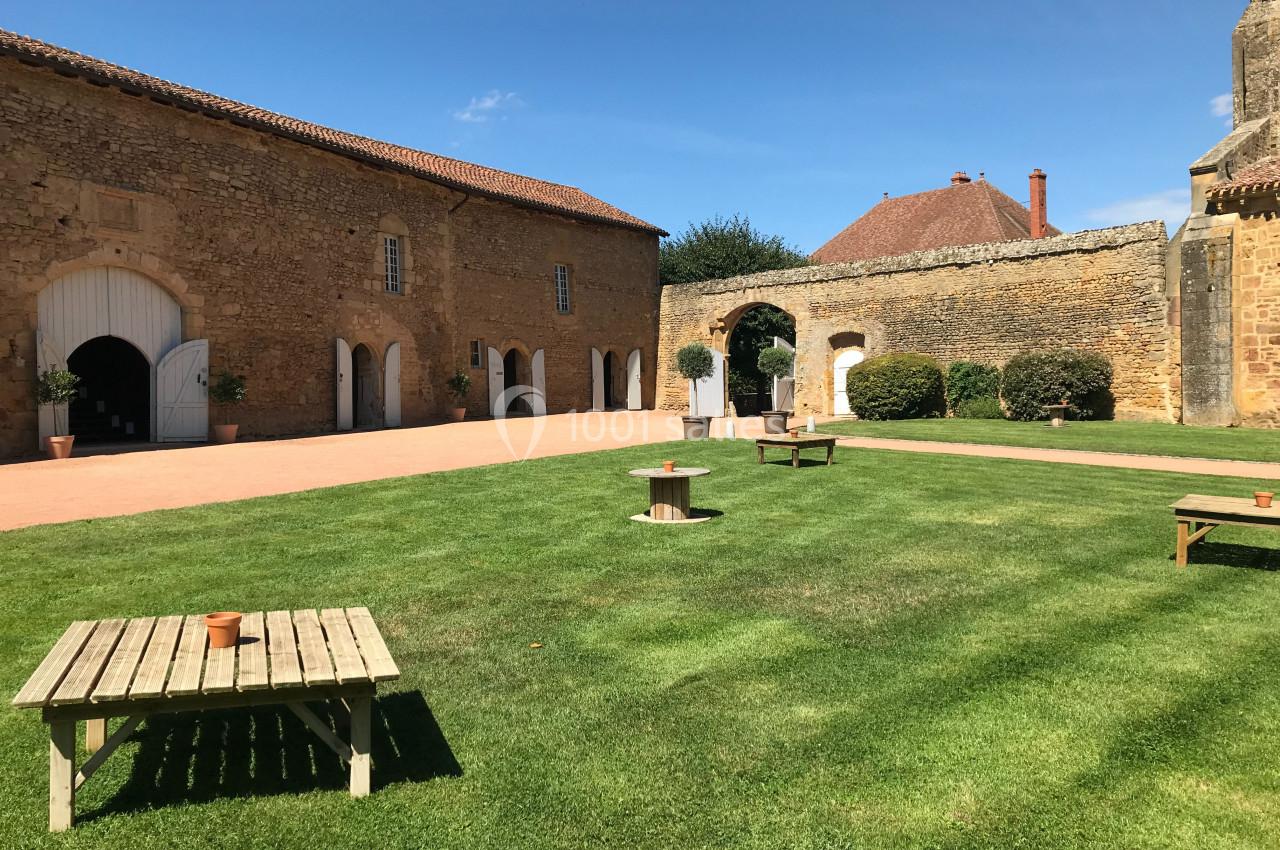 Cour intérieure avec pelouse, bancs en bois, bâtiments en pierre et ciel dégagé en arrière-plan.