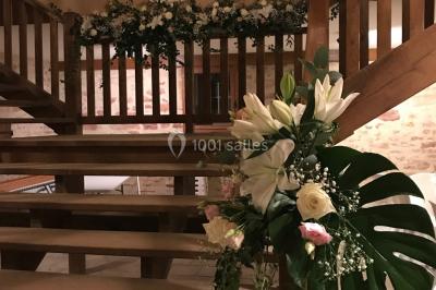 Église illuminée de nuit avec un clocher éclairé, vue depuis une allée avec des braseros allumés au premier plan.