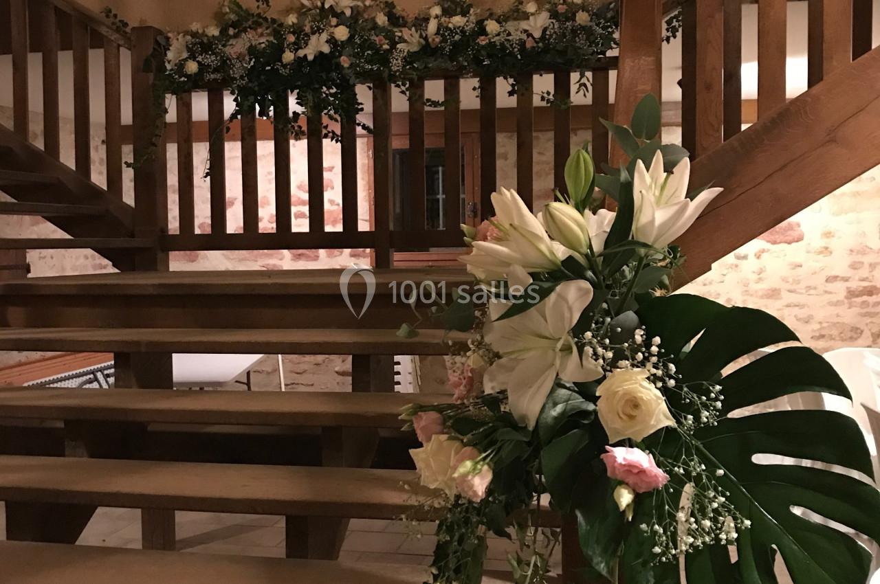 Escalier en bois décoré de fleurs blanches et roses avec feuillage, dans une salle aux murs en pierre apparente.