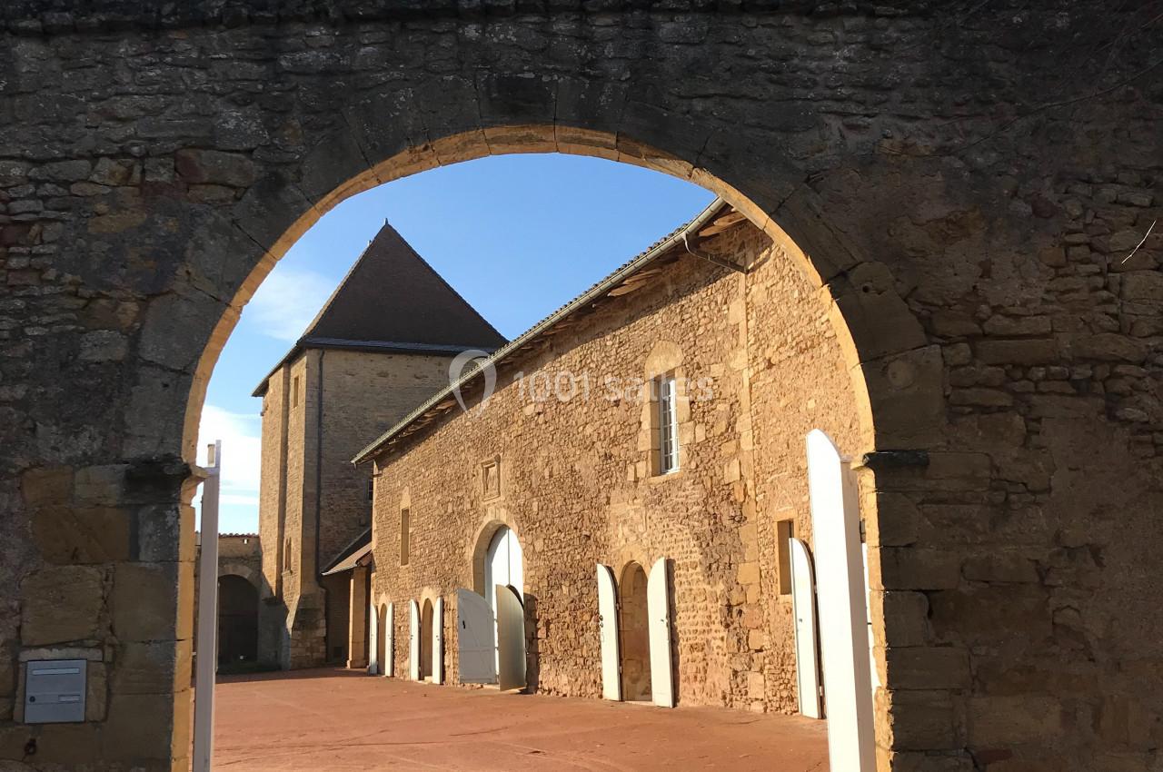 Vue d'une cour intérieure ensoleillée avec des bâtiments en pierre et une arche en premier plan.