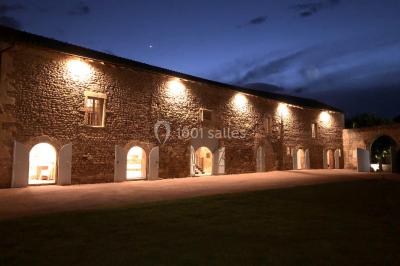 Église illuminée de nuit avec un clocher éclairé, vue depuis une allée avec des braseros allumés au premier plan.