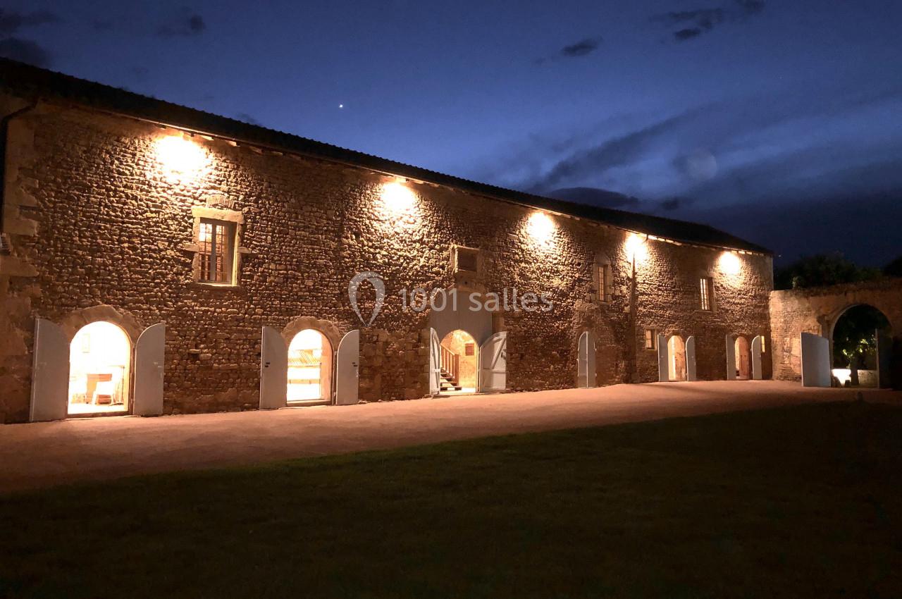 Façade en pierre d'un bâtiment éclairé la nuit, avec des portes et fenêtres ouvertes sur une cour.
