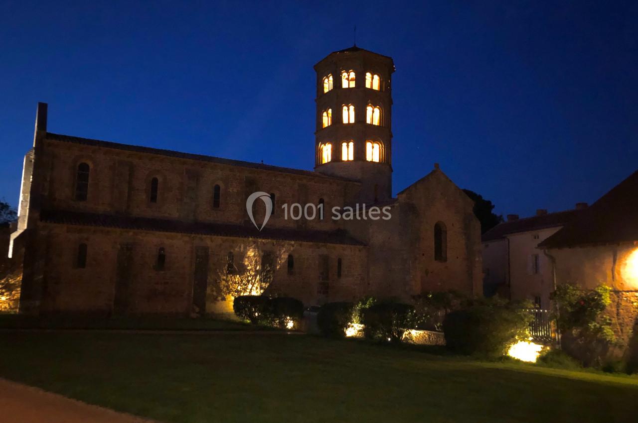 Église en pierre éclairée la nuit, avec un clocher illuminé et un jardin à l'avant.