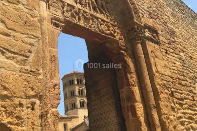 Église illuminée de nuit avec un clocher éclairé, vue depuis une allée avec des braseros allumés au premier plan.