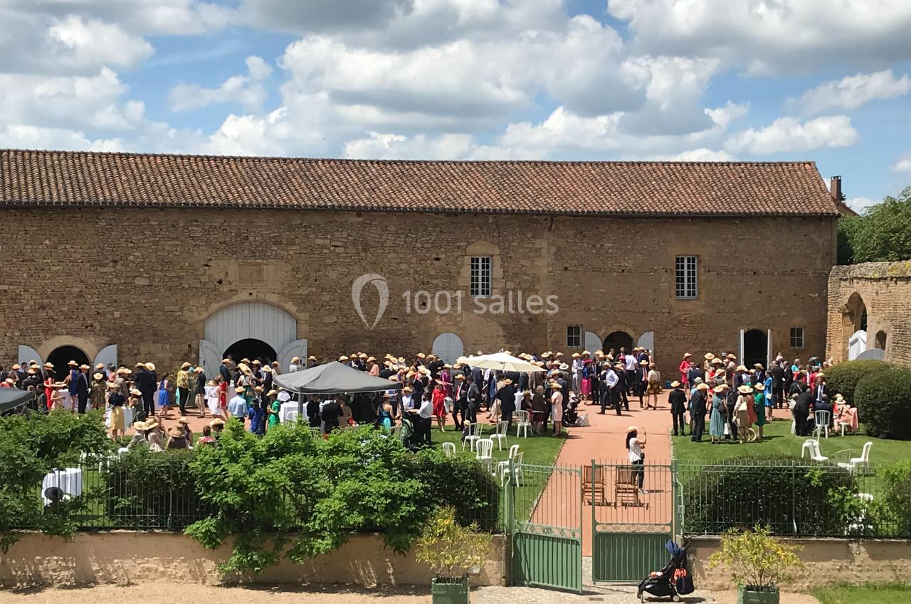 Groupe de personnes rassemblées dans une cour devant un bâtiment en pierre sous un ciel partiellement nuageux.