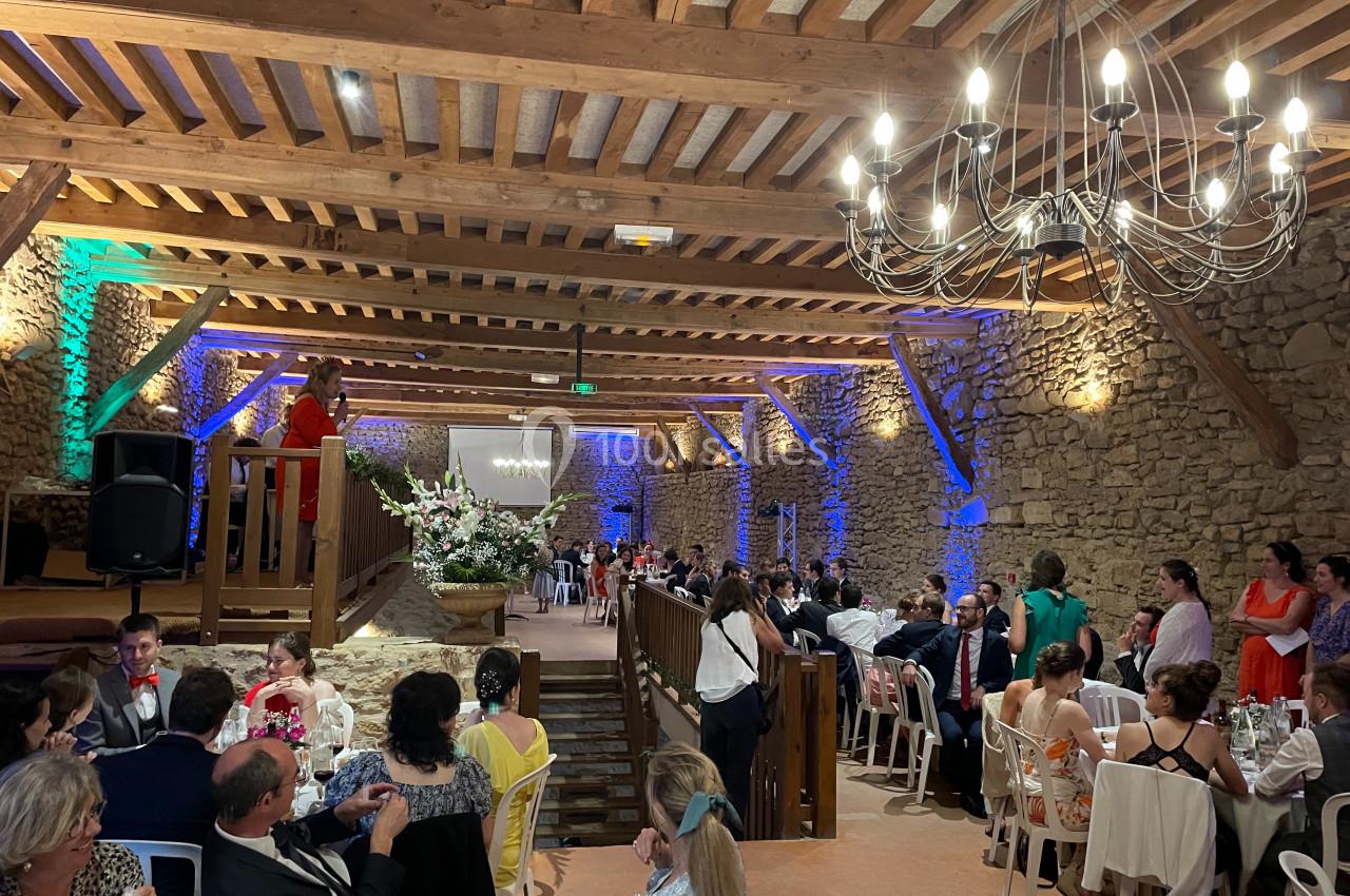 Salle de réception en pierre avec des invités assis, un discours en cours sur une estrade et un éclairage chaleureux.