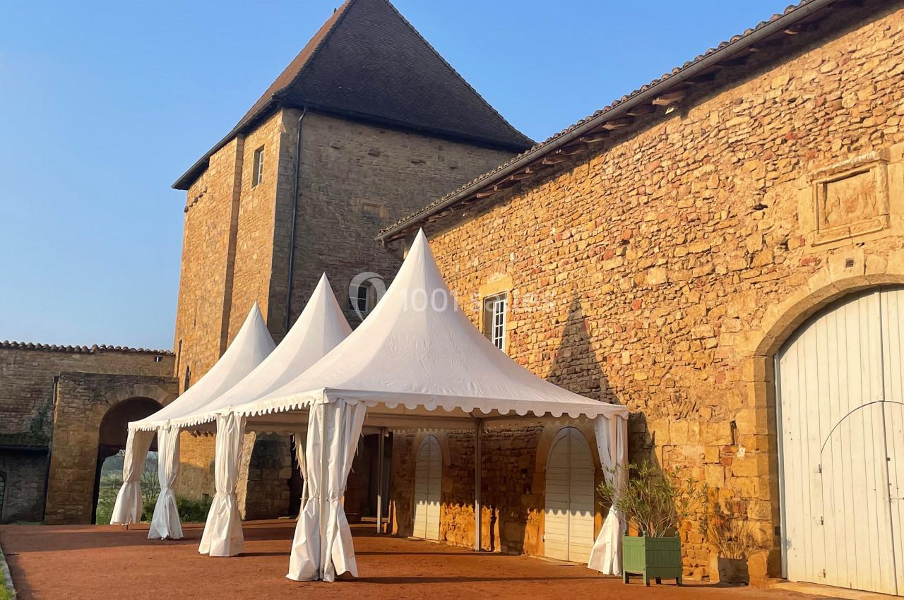 Tentes blanches installées devant un bâtiment en pierre avec une grande porte en bois, sous un ciel dégagé.