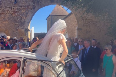 Église illuminée de nuit avec un clocher éclairé, vue depuis une allée avec des braseros allumés au premier plan.