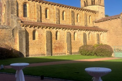 Église illuminée de nuit avec un clocher éclairé, vue depuis une allée avec des braseros allumés au premier plan.