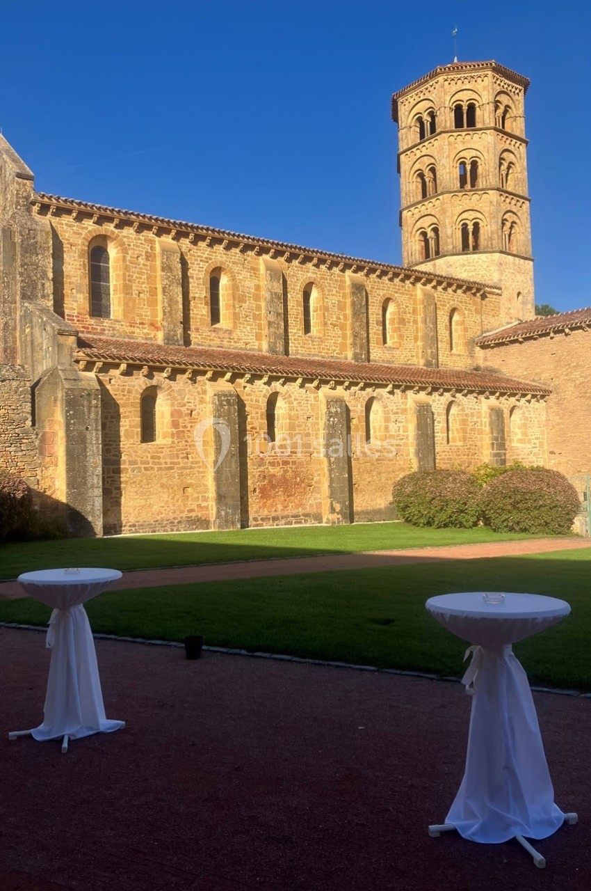 Façade en pierre d'une église romane avec une tour, vue depuis une cour avec des tables hautes drapées de blanc.
