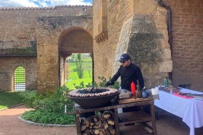 Église illuminée de nuit avec un clocher éclairé, vue depuis une allée avec des braseros allumés au premier plan.