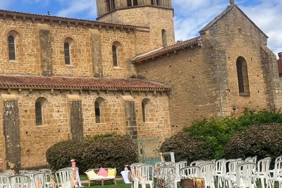 Église illuminée de nuit avec un clocher éclairé, vue depuis une allée avec des braseros allumés au premier plan.