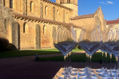 Église illuminée de nuit avec un clocher éclairé, vue depuis une allée avec des braseros allumés au premier plan.
