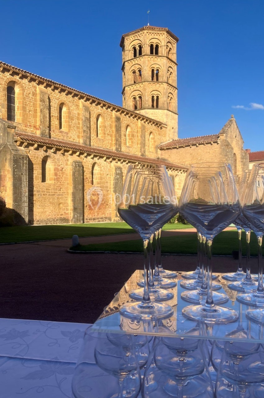 Vue d'une abbaye en pierre sous un ciel bleu, avec des verres à pied disposés sur une table au premier plan.