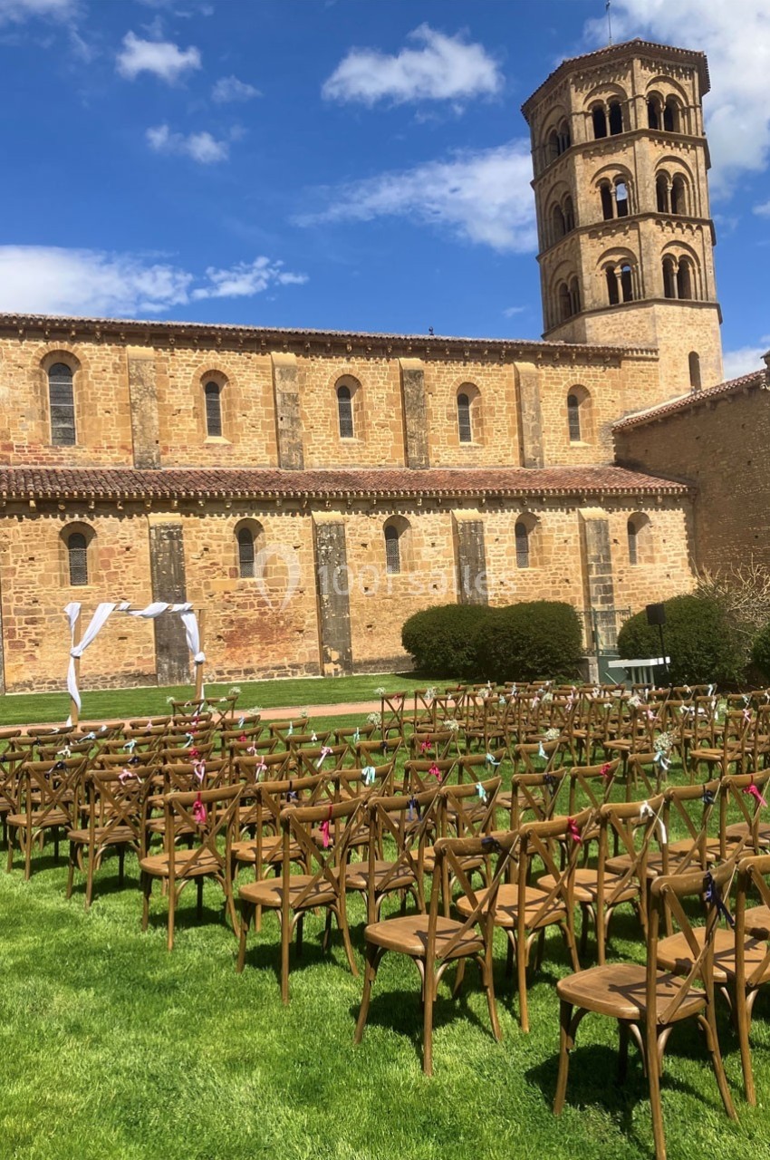 Chaises disposées en rangées sur une pelouse devant une église en pierre, préparées pour une cérémonie en plein air.