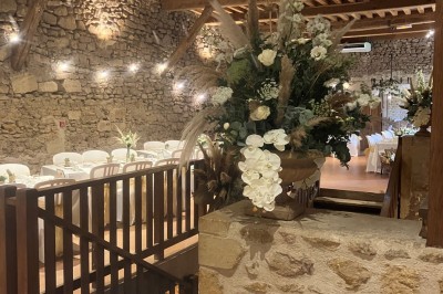 Église illuminée de nuit avec un clocher éclairé, vue depuis une allée avec des braseros allumés au premier plan.